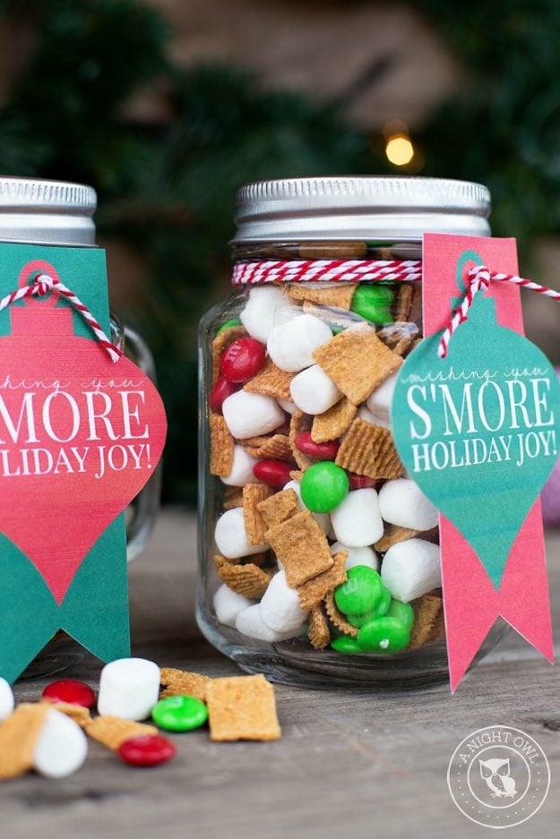 Two mason jars of s'mores snack mix with Golden Grahams, mini marshmallows and red and green candies, tied with baker's twine and ornament gift tags