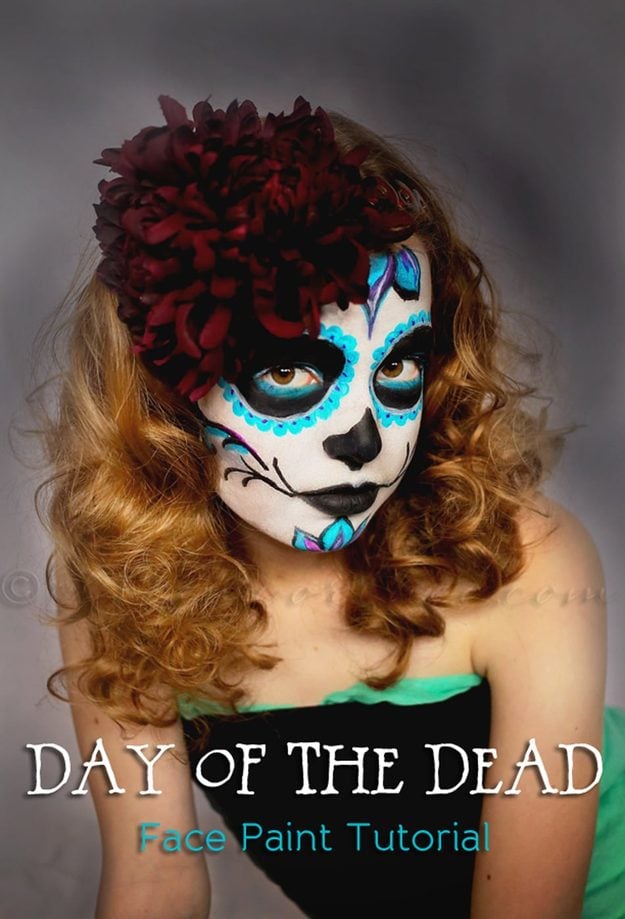 Sugar skull Halloween makeup with blue eye petals, black face paint and red flowers in long curled hair