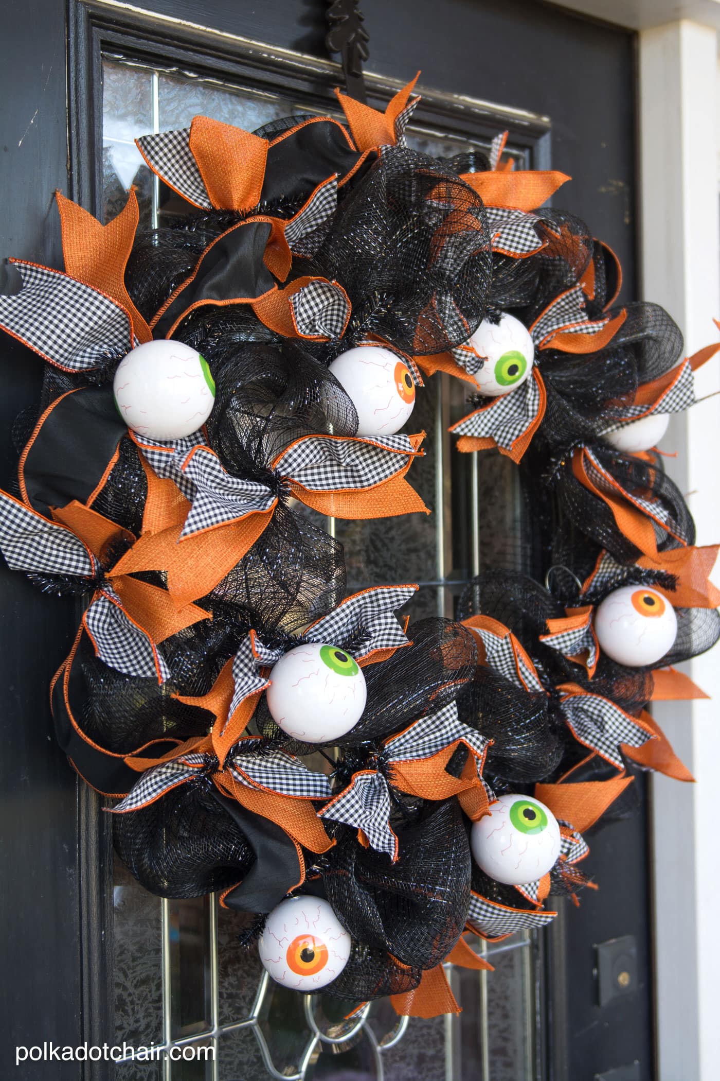 Black geo mesh Halloween wreath with orange gingham ribbon, eyeball ornaments and Polka Dot Chair watermark on a door