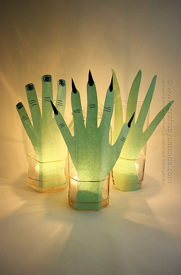 Green paper hands wrap around tall glass jars with flameless lights in a spooky Halloween tabletop display