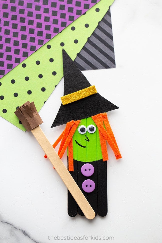 Finished green popsicle stick witch with black hat, orange yarn hair, buttons and a small brown paper broom
