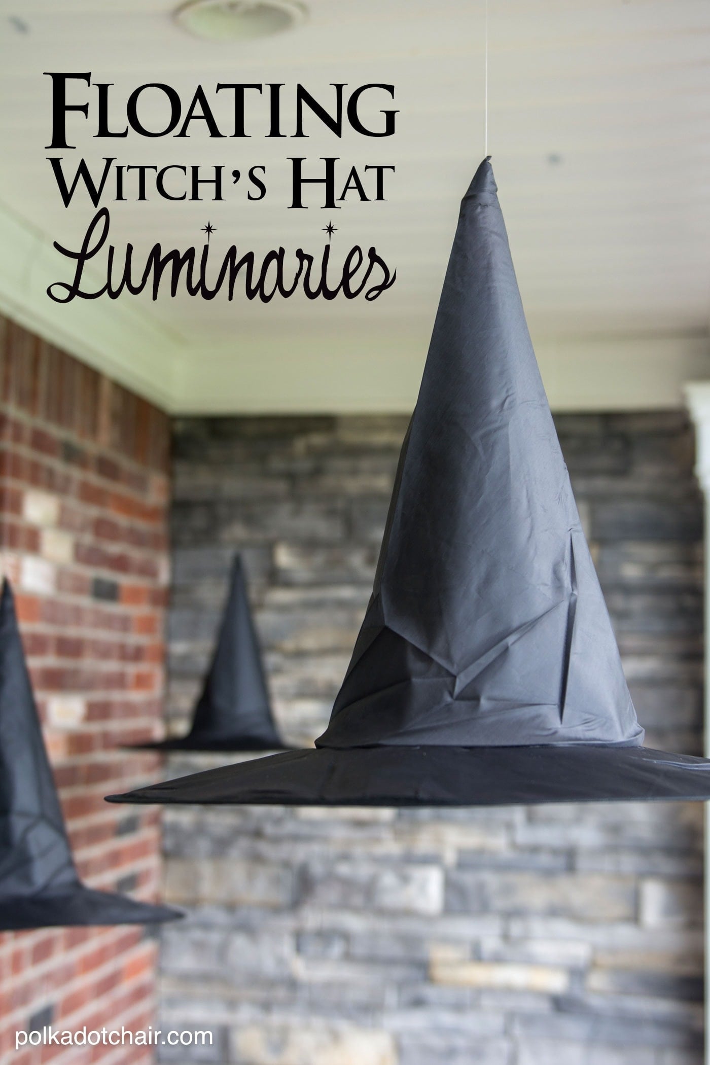 Black witch hats hang outdoors with battery lights glowing beneath them and a Polka Dot Chair watermark