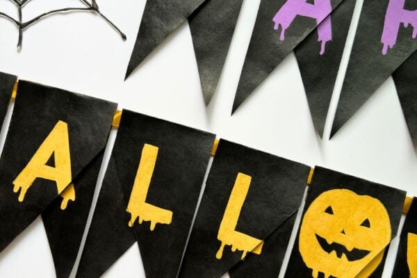 Black Happy Halloween banner made from painted toilet roll pieces hangs on ribbon with a pumpkin letter