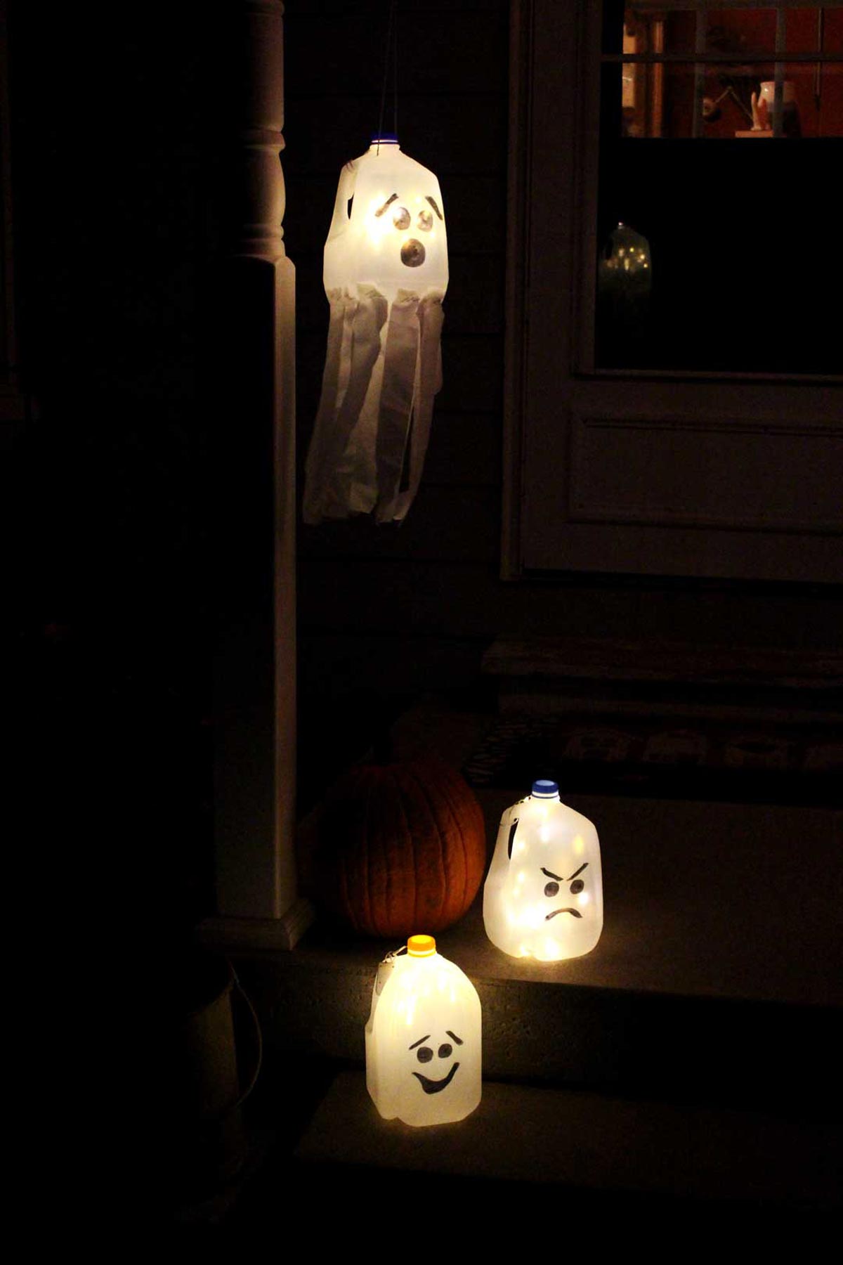 Three recycled milk jug ghosts glow with battery lights at night and show different black marker faces