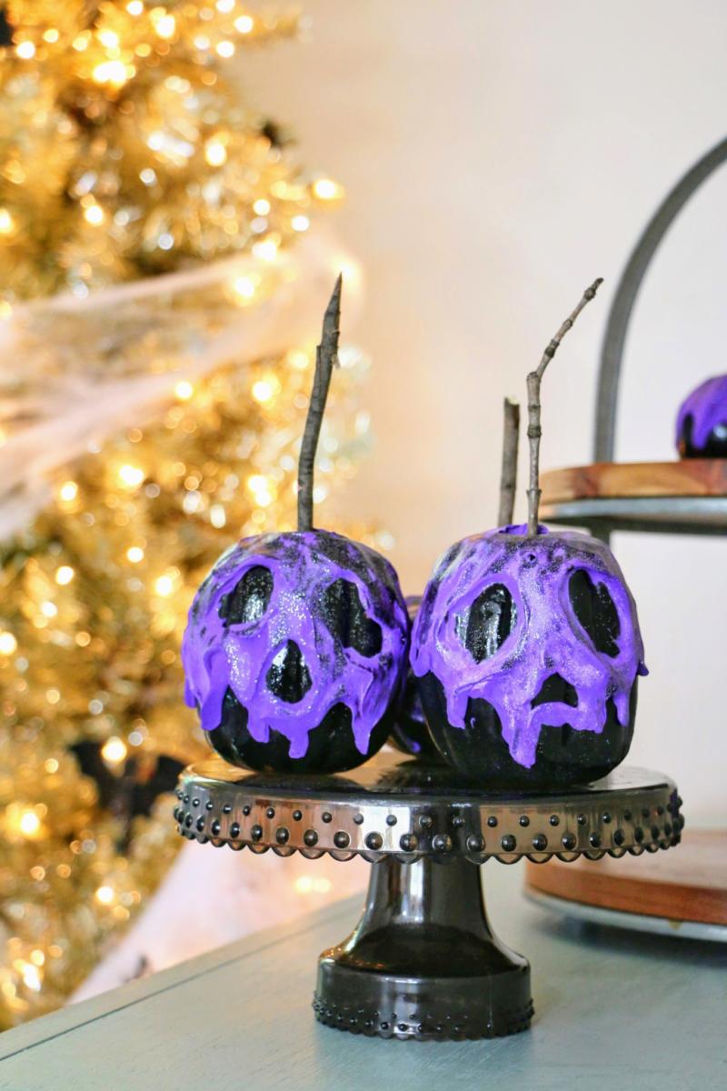 Two black foam pumpkins with molded purple poison apple faces and glitter details sit on a dark pedestal