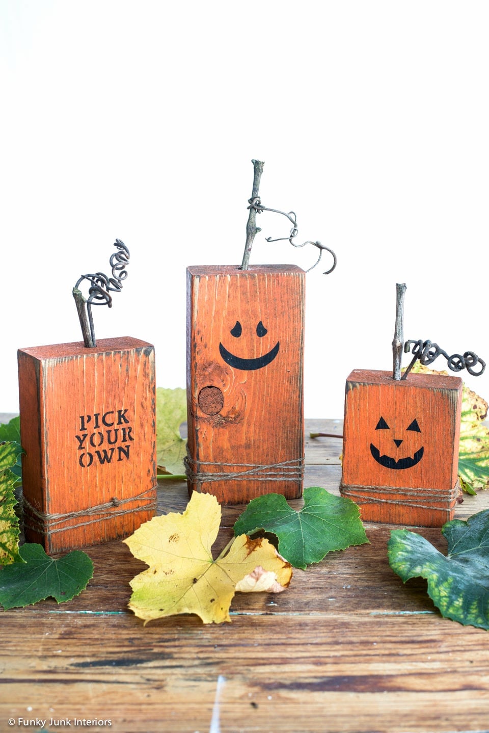 Three orange scrap wood pumpkins with black faces, rustic distressing, branch stems and copyright mark