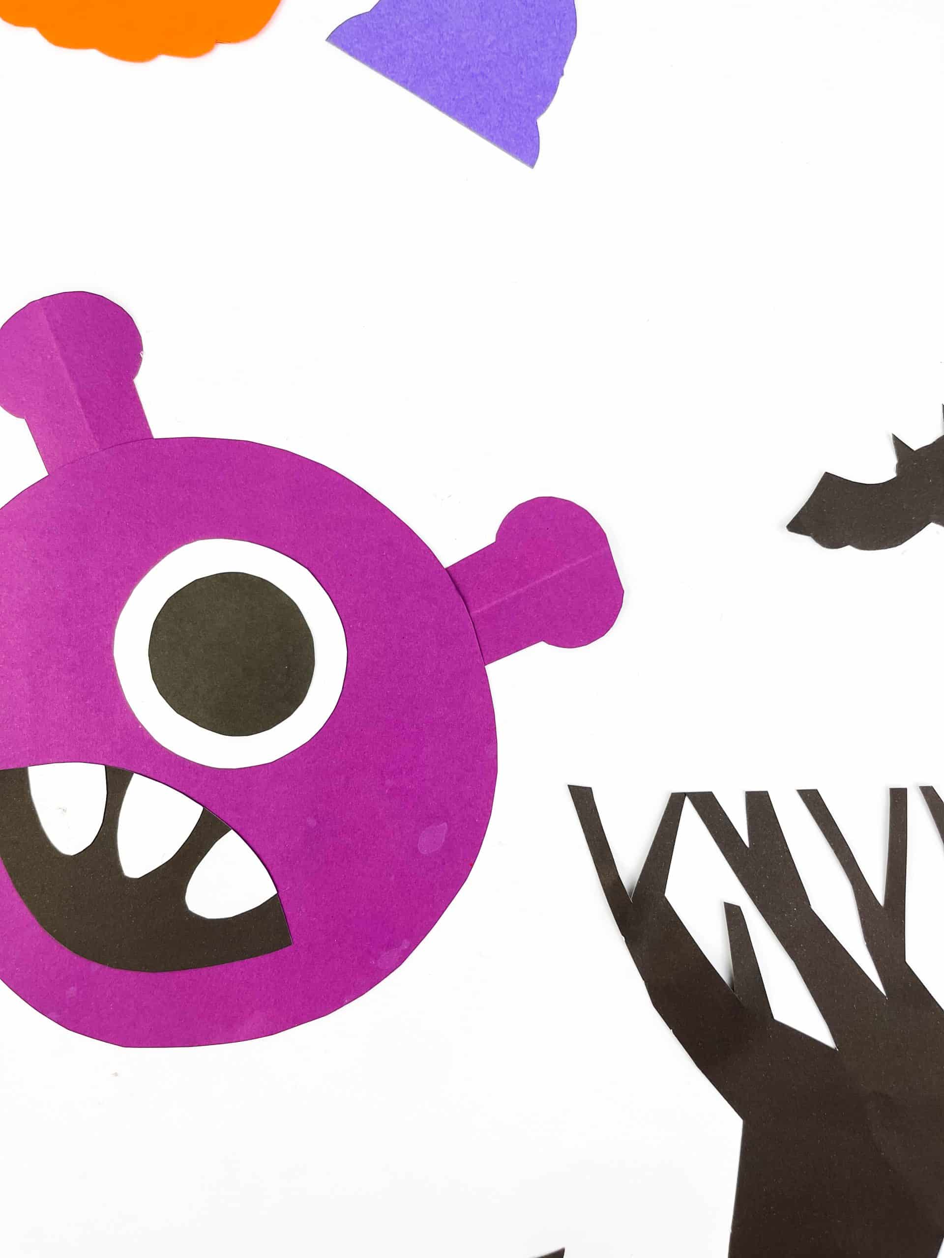 Purple paper rocking monster with horns, teeth, one eye and small Halloween shapes stands in a paper scene