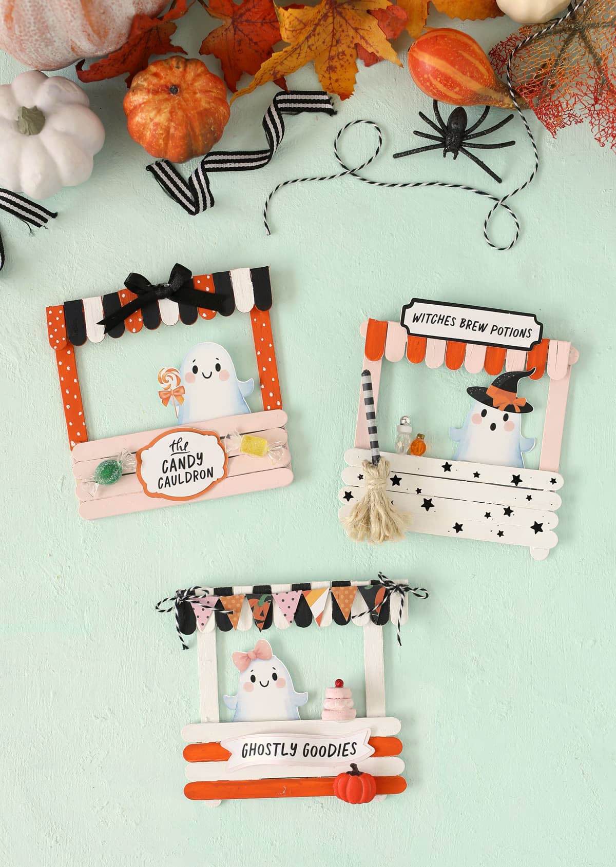 Three finished popsicle stick Halloween storefronts display painted signs, awnings and tiny decorations