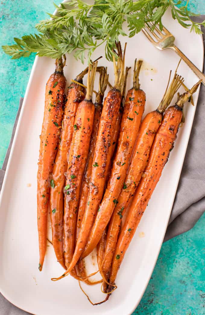 Slow Cooker Glazed Carrots Recipe Glazed whole carrots arranged on a white rectangular platter over a turquoise surface in a finished side dish