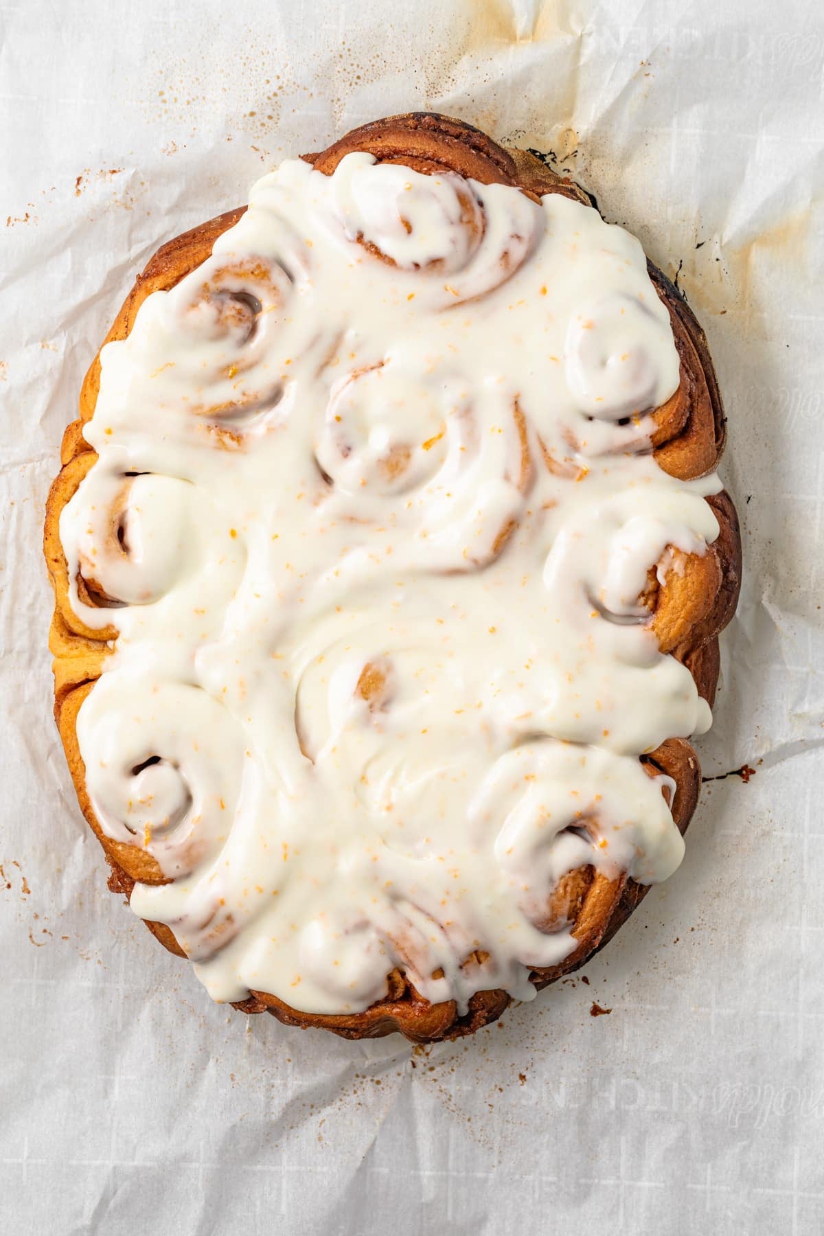 Slow Cooker Orange Sweet Rolls Orange sweet rolls baked together on parchment and covered with an orange-speckled glaze in a finished view