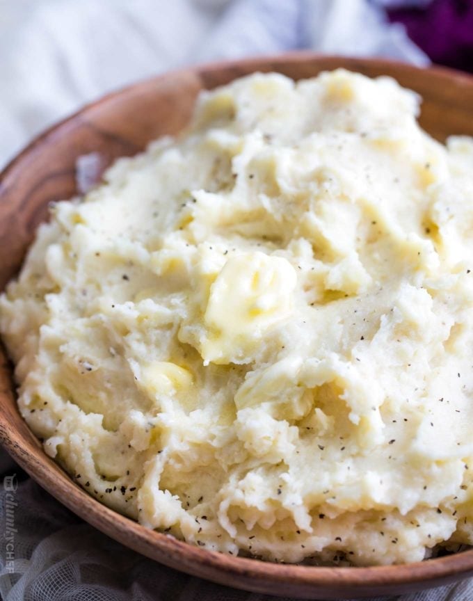 Homestyle Crockpot Mashed Potatoes Creamy mashed potatoes with butter and pepper in a wooden bowl as a finished crockpot Thanksgiving side dish