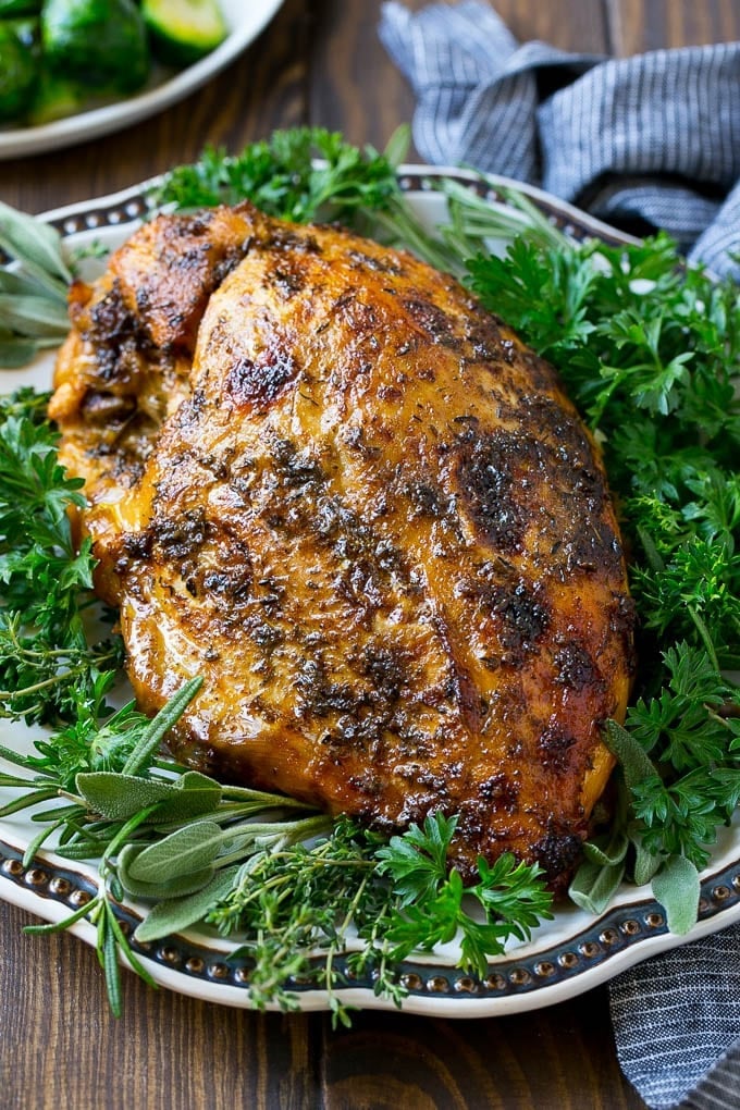 Herb-Crusted Slow Cooker Turkey Breast Browned herb-coated turkey breast on a serving platter surrounded by parsley, sage, rosemary and thyme