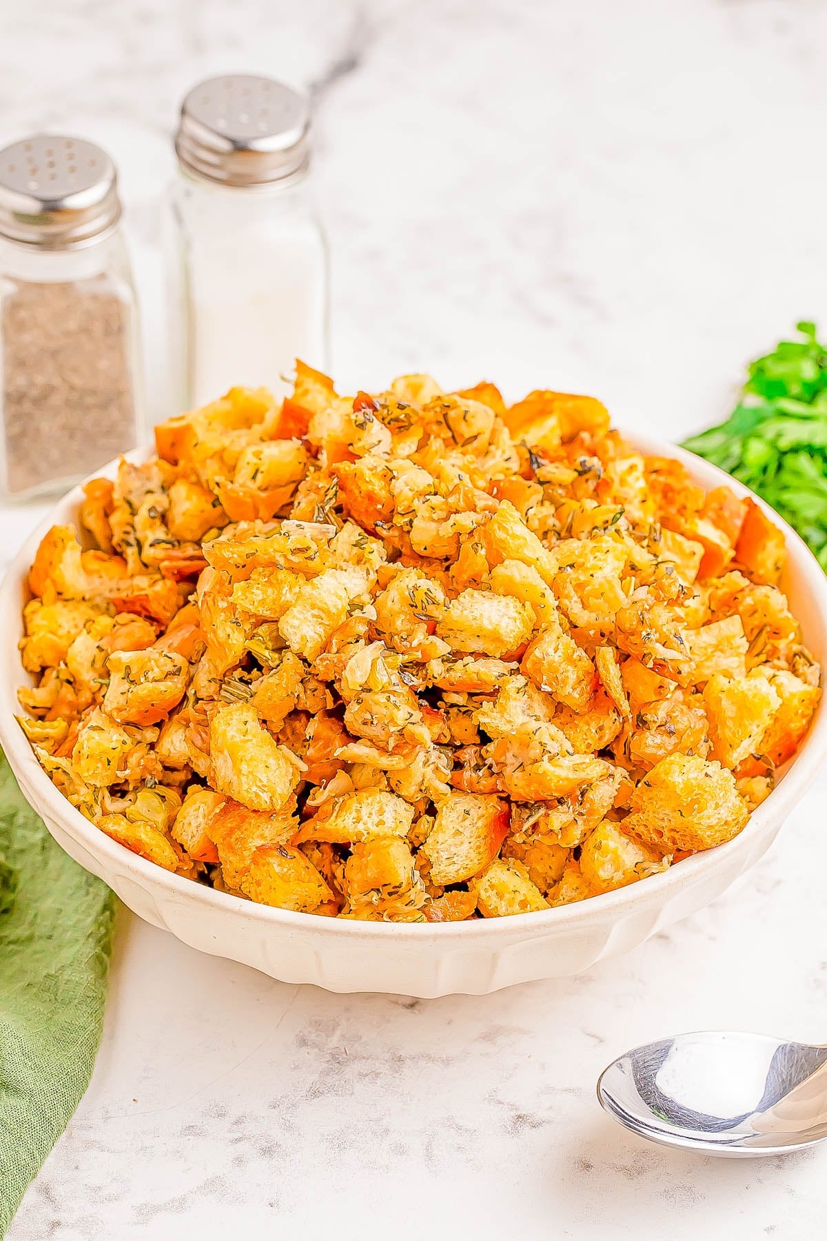 Easy Slow Cooker Stuffing Recipe Herb stuffing in a white bowl with parsley, serving spoon, salt and pepper shakers and a green cloth