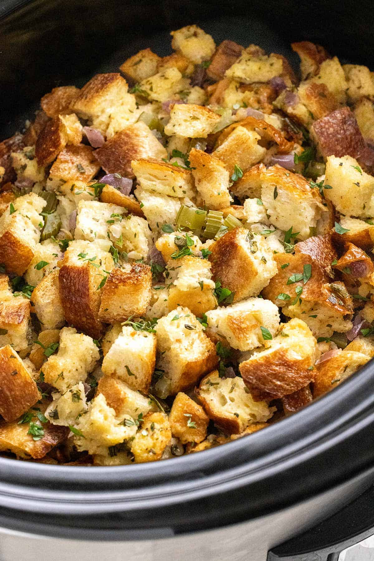 Crock Pot Stuffing With Herbs Recipe Golden bread-cube stuffing with celery, red onion and herbs fills a black slow-cooker insert in a close-up