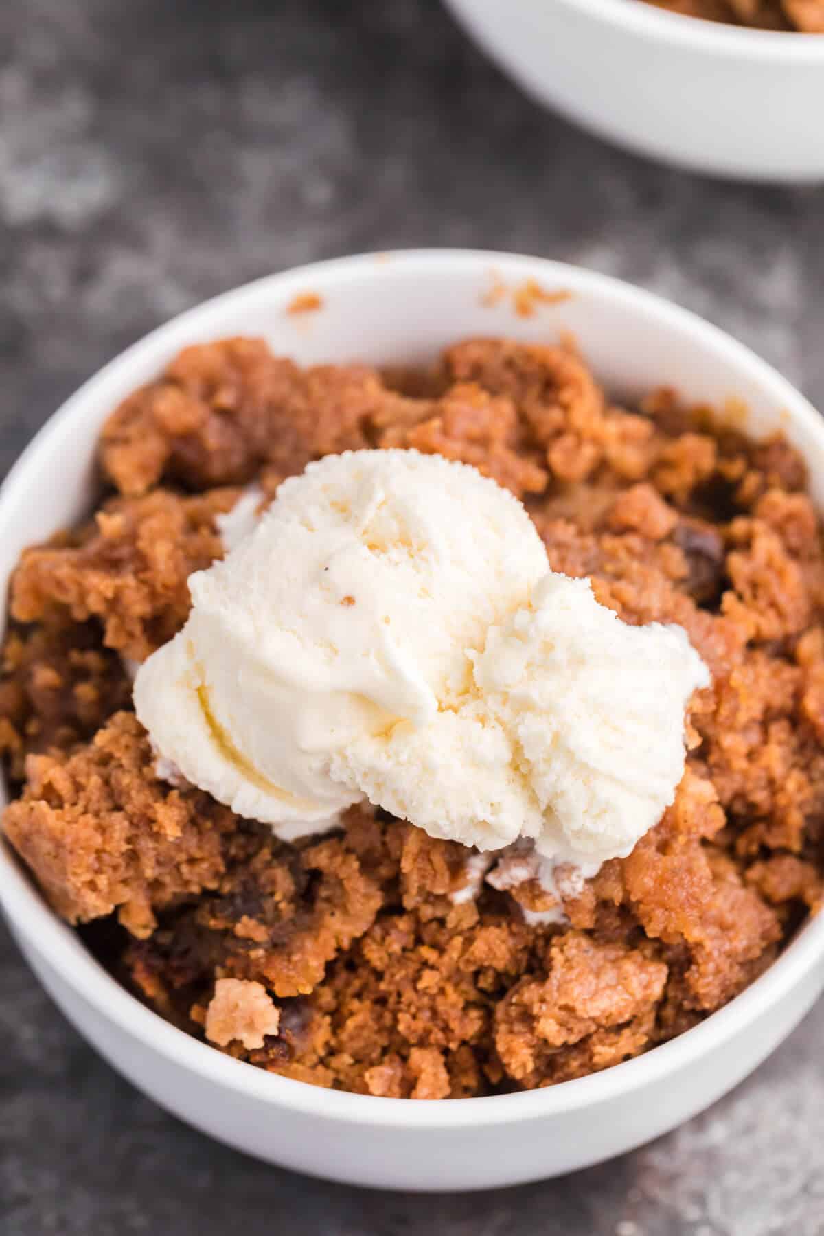 Easy Slow Cooker Pumpkin Dump Cake Pumpkin dump cake in a white bowl topped with vanilla ice cream as a finished slow cooker holiday dessert