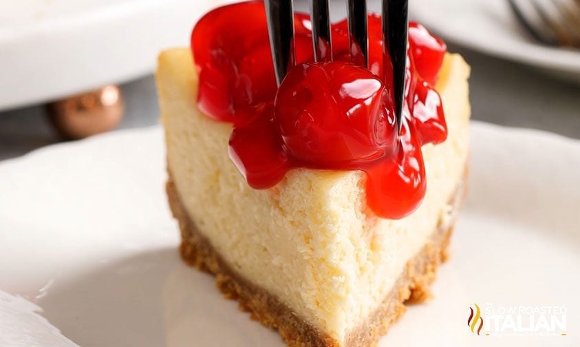 Best Crock Pot Creamy Cheesecake Plain cheesecake slice topped with glossy cherry sauce on a white plate in a finished dessert close-up