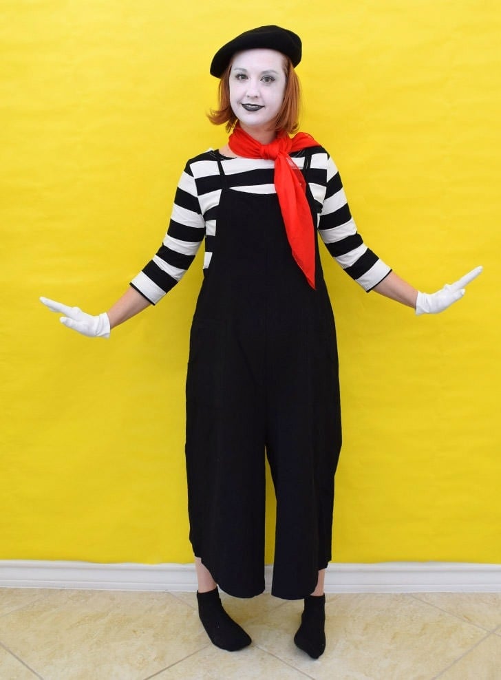 Adult wearing a striped mime costume with black overalls, beret, red kerchief, white gloves and theatrical face makeup