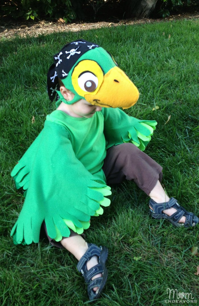 Child wearing a Skully parrot costume with green fleece wings, layered felt feathers and a matching pirate cap