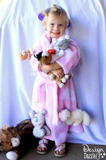 Child wearing a pink bathrobe covered with plush cats and purple hair rollers in a Cat Lady costume with source watermark