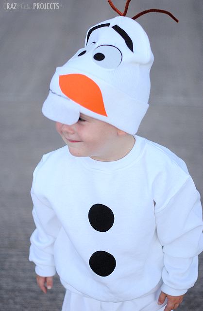 Child wearing a white Olaf sweatshirt with black buttons and a character hat with orange nose and brown twigs