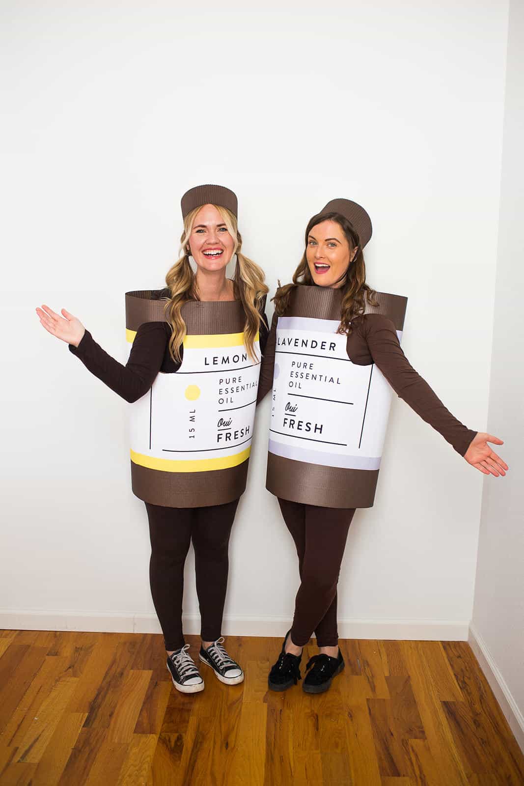 Two women wearing brown essential oil bottle costumes labeled lemon and lavender with matching cap headpieces