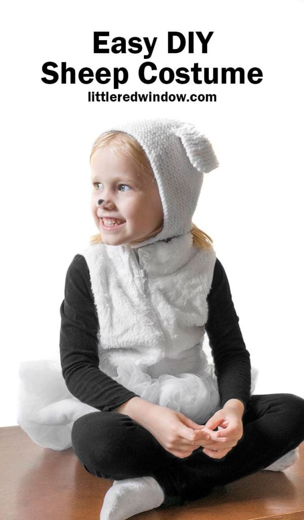 Child wearing a white sherpa sheep costume with black clothes, a tulle tail and a knitted hood with floppy ears
