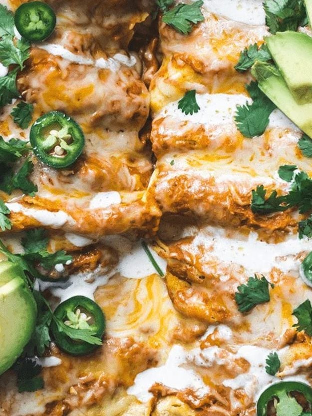 Pan of pumpkin sauce enchiladas topped with melted cheese, jalapeno slices, avocado and fresh cilantro