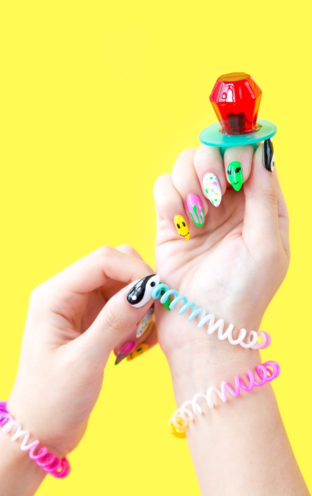 90s Throwback Manicure | Quick Nail Art Idea 90s throwback manicure with smiley face, alien, slime drip, paint splatter and yin yang nails on hands holding a ring pop