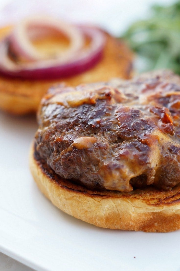 Bacon and cheddar stuffed hamburger patty with melted cheese on a toasted bun with red onion
