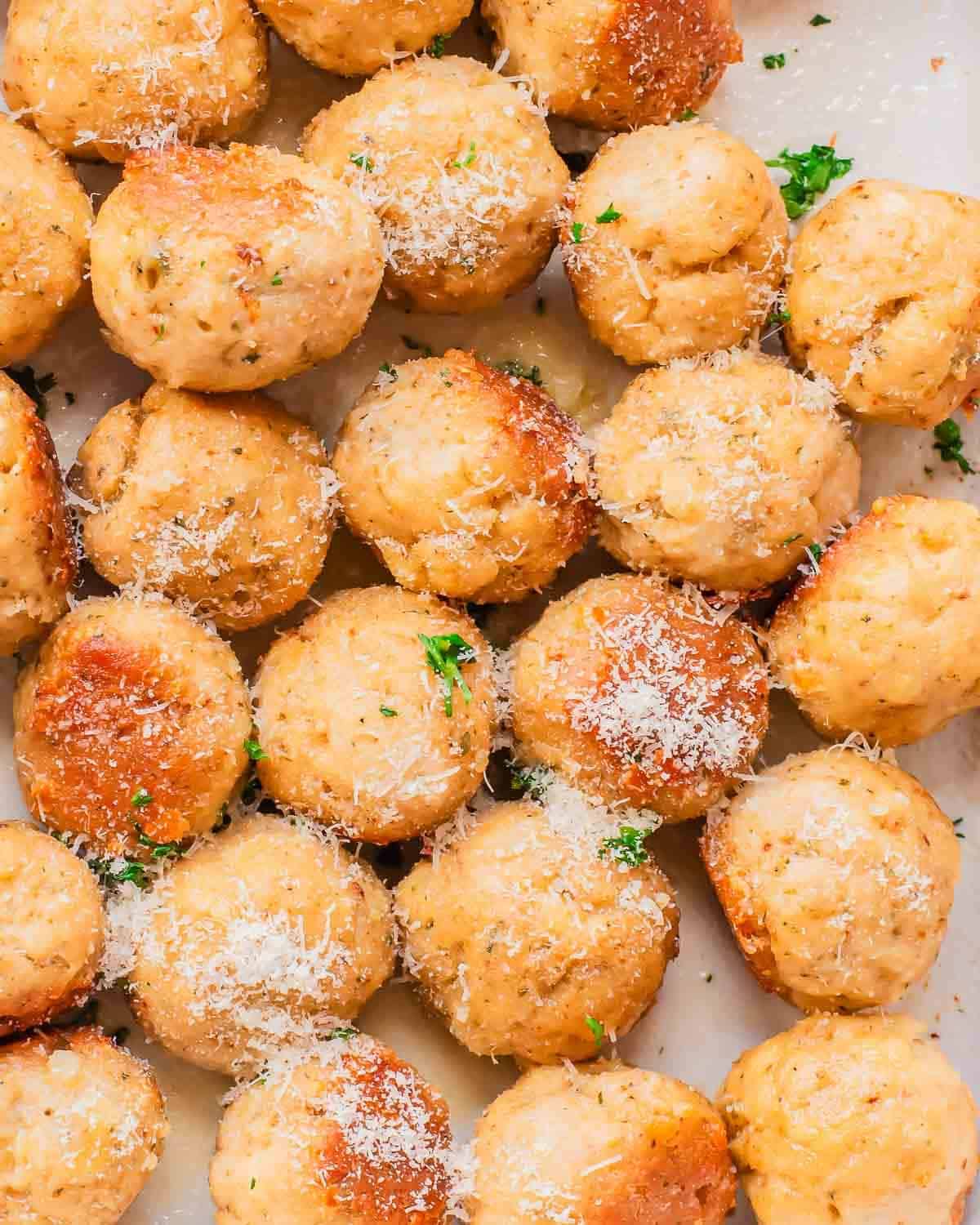 Golden baked chicken meatballs dusted with grated Parmesan and parsley on a baking sheet