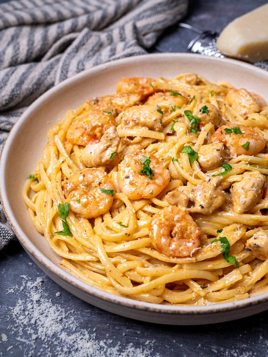 Bowl of creamy Cajun linguine with seared shrimp and chicken pieces topped with parsley