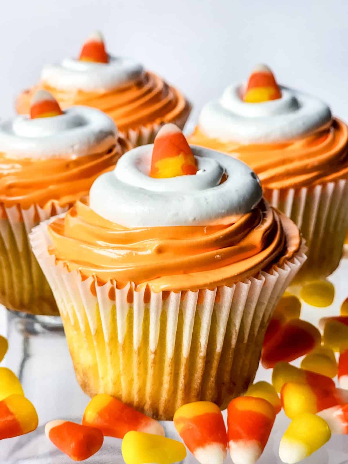Cupcakes with orange star-piped frosting and a round white frosting top, each with a piece of candy corn