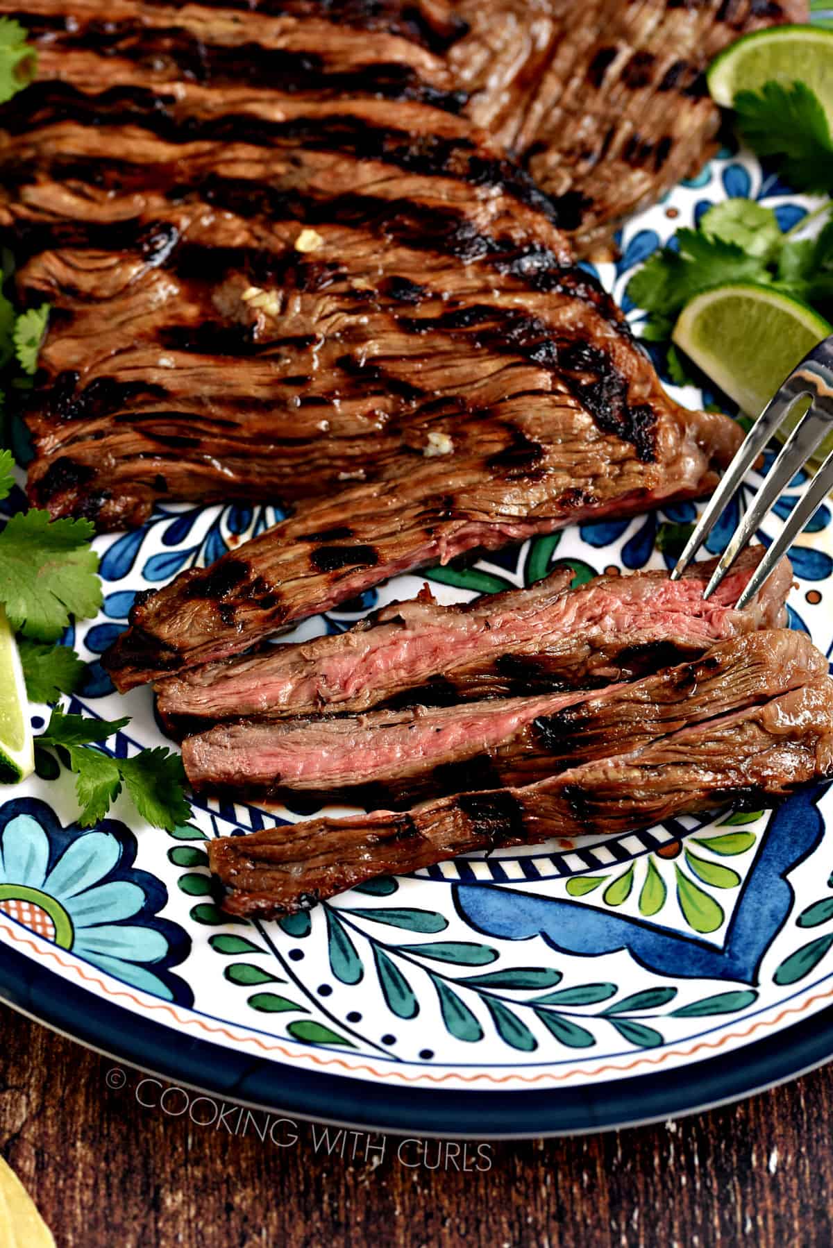 Carne Asada Sliced grilled carne asada skirt steak with dark grill marks on a blue and white patterned plate with lime wedges and cilantro