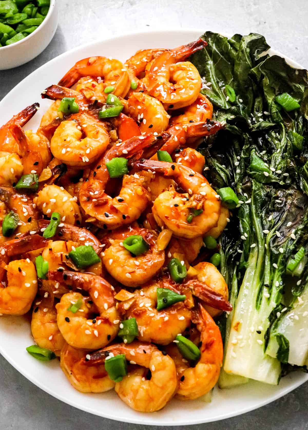 Platter of glazed chili garlic shrimp with green onion and sesame seeds beside roasted baby bok choy