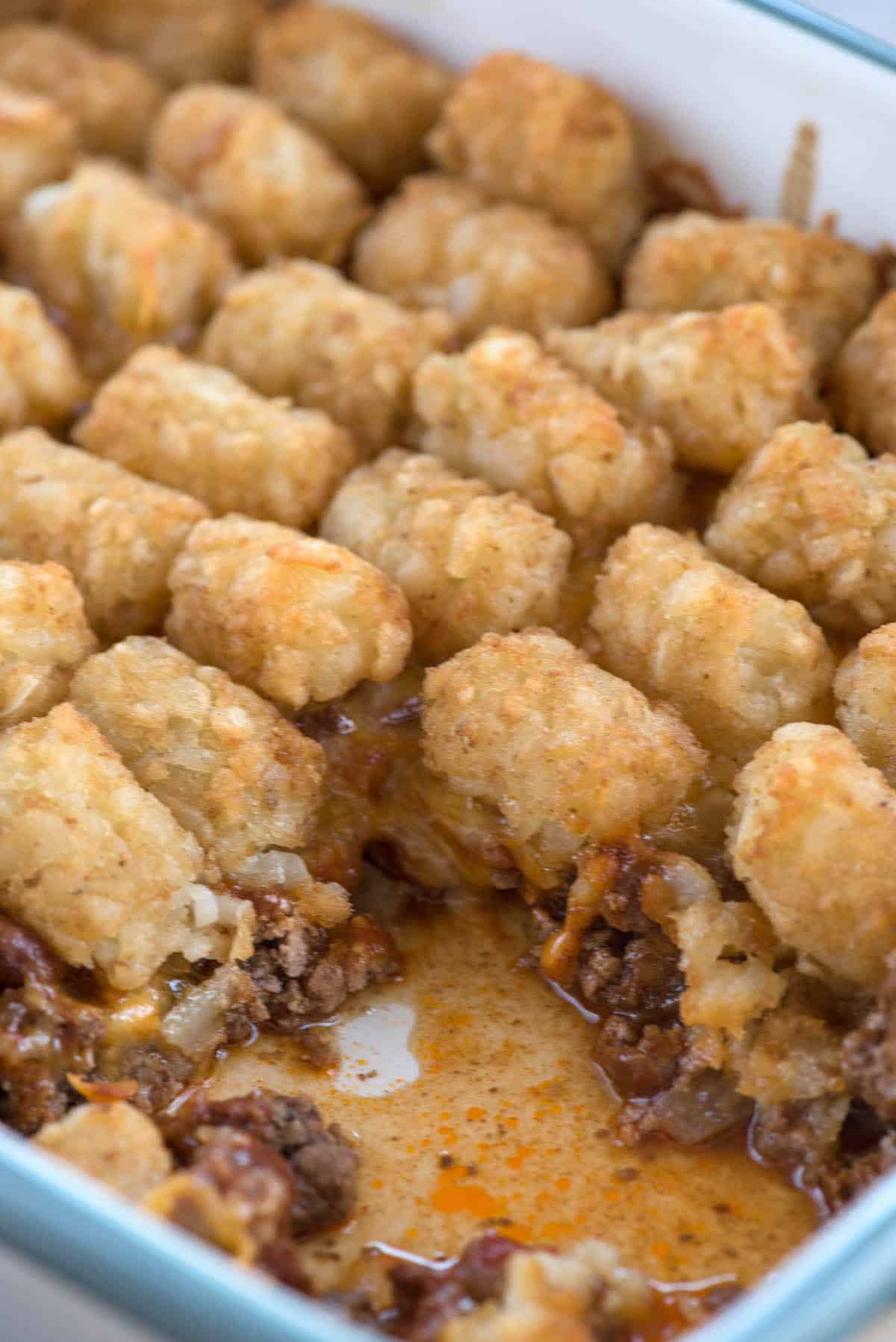Baking dish of chili tater tot casserole with a scoop removed to show beef chili under crispy tots