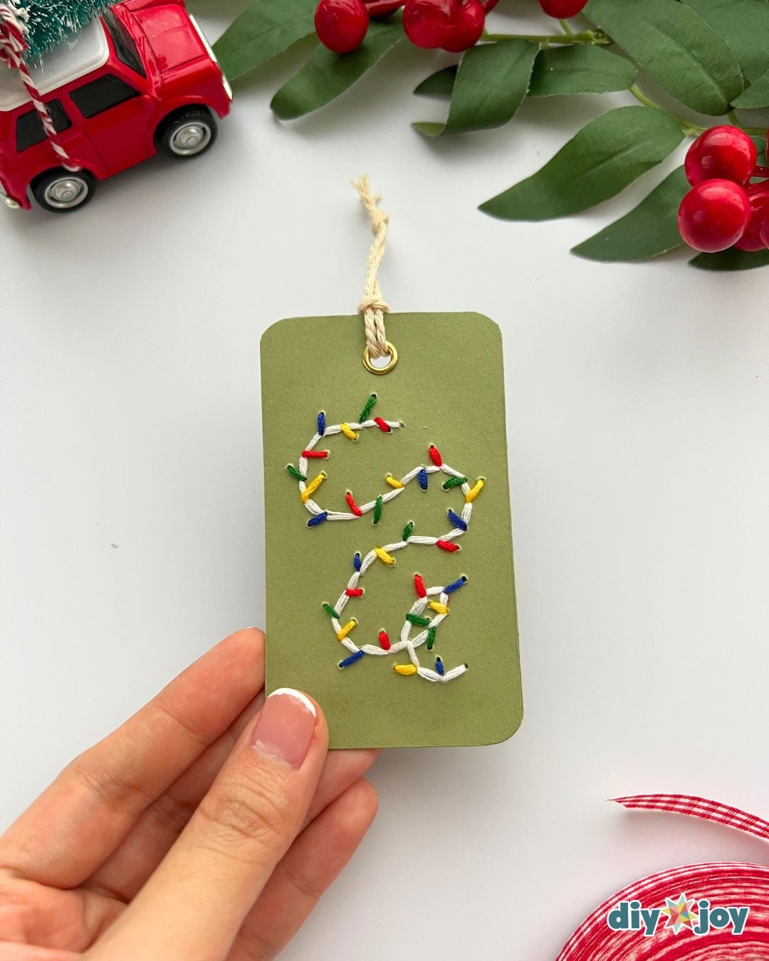 Christmas paper crafts - hand holding a green embroidered gift tag with a colorful Christmas lights design