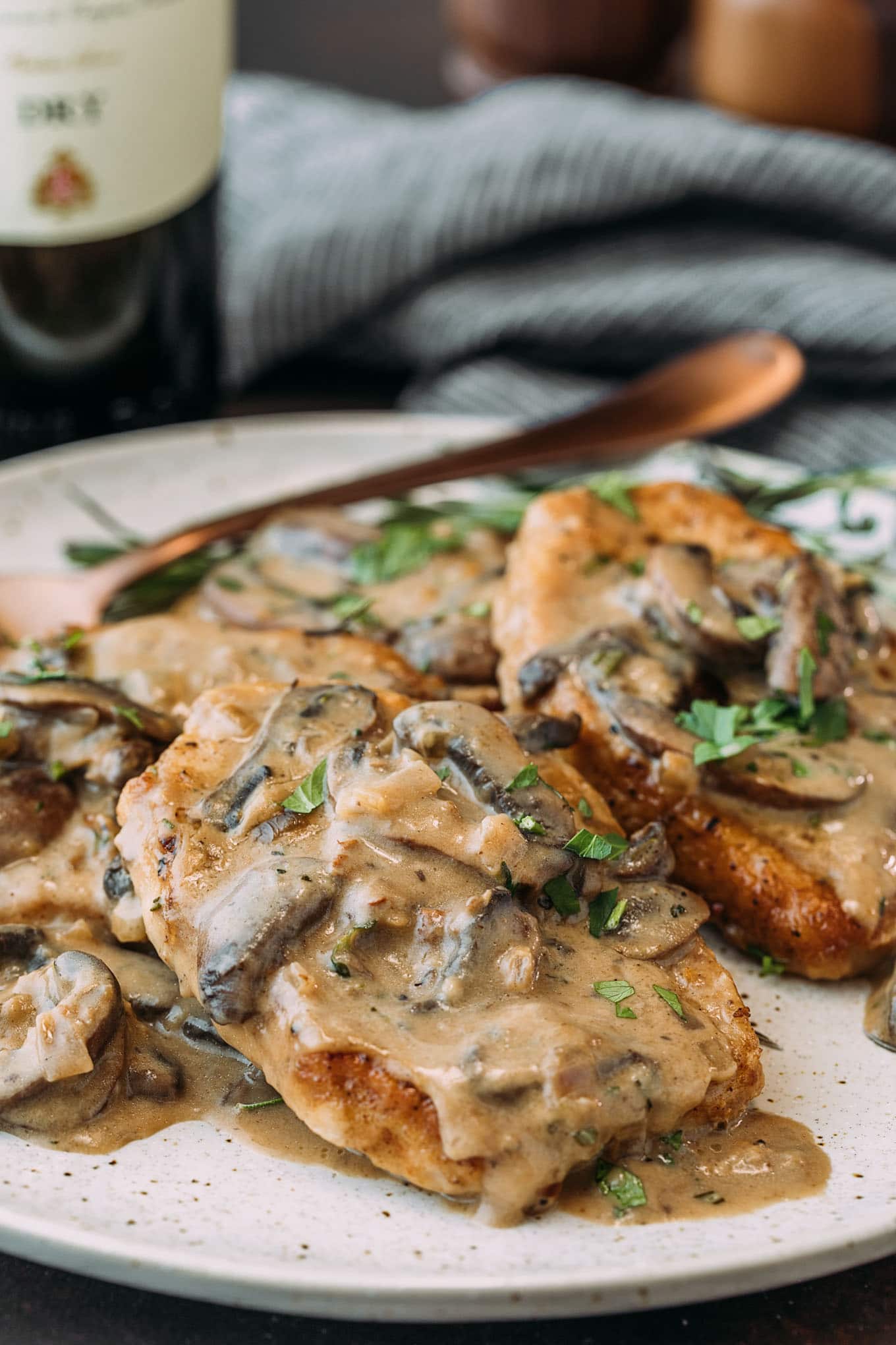 Thin pork chops in creamy mushroom Marsala sauce with fresh herbs on a white plate