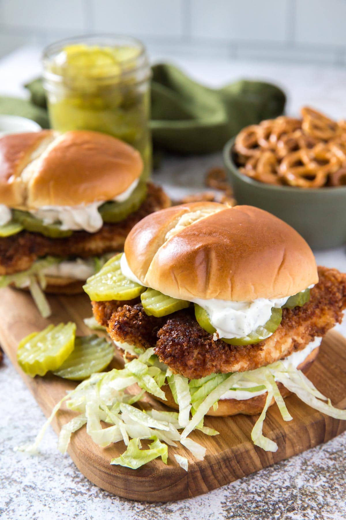 Two crispy chicken sandwiches with pickles, creamy sauce and shredded lettuce on a wooden board