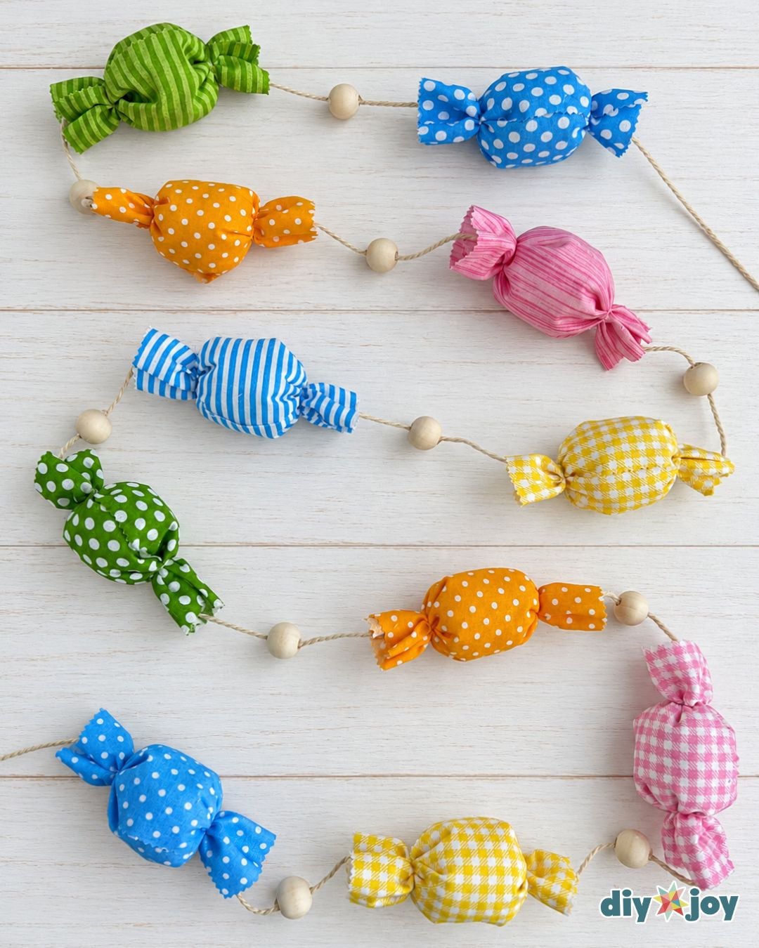 Colorful fabric candy garland with wooden beads snaking across white wood planks, made from leftover fabric scraps