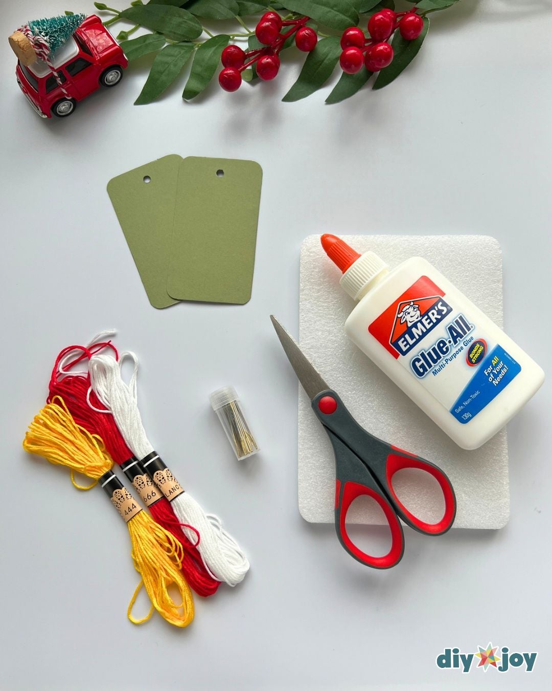 Embroidery gift tag supplies - cardstock tags, embroidery thread, needle, scissors and glue laid out on a foam mat