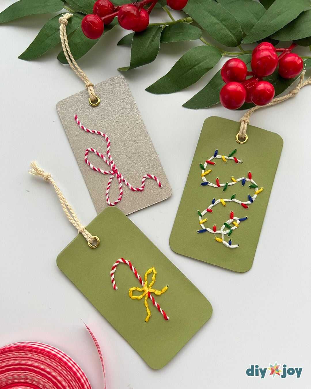 DIY embroidered gift tags - three finished tags in green and kraft cardstock lying flat with holly and ribbon