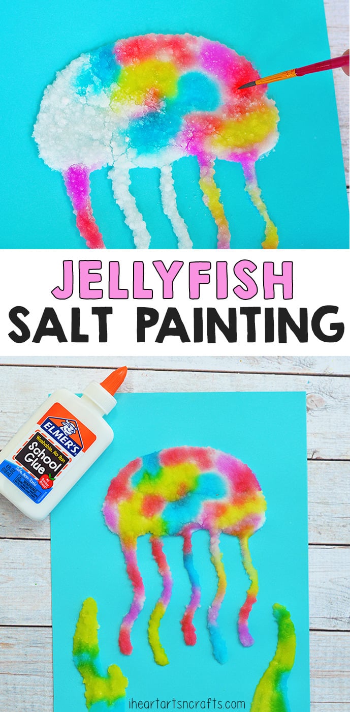Pink and yellow jellyfish salt painting on blue cardstock with trailing tentacles, beside a school glue bottle