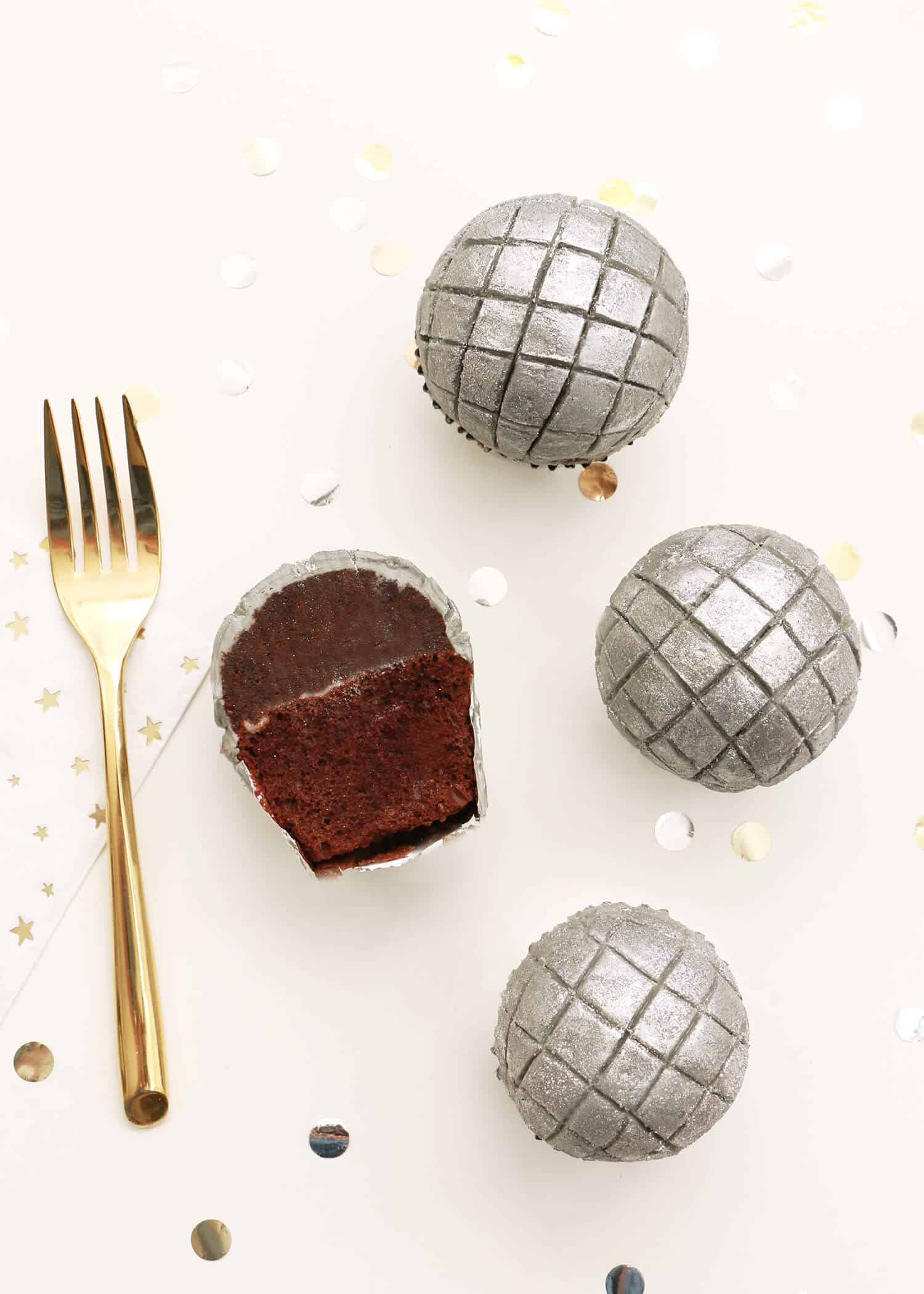 Dome-shaped silver cupcakes scored in a grid like disco balls, one cut open to show chocolate cake, gold fork