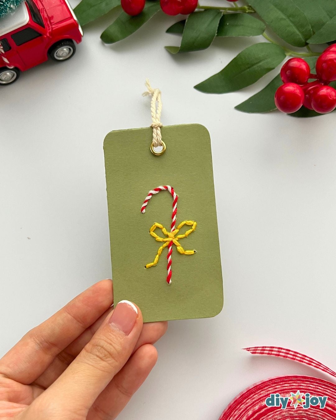 Easy Christmas crafts - green cardstock tag with an embroidered candy cane and yellow bow held up to the camera