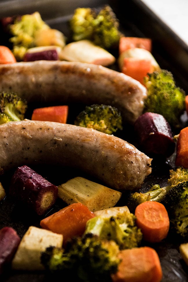 Roasted sausages on a sheet pan with chunks of carrots, parsnips and broccoli