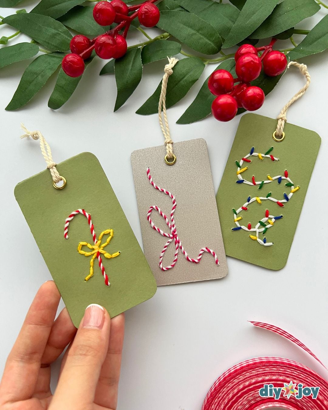 DIY embroidery gift tags - hand holding three stitched Christmas tags with candy cane, bow and lights designs