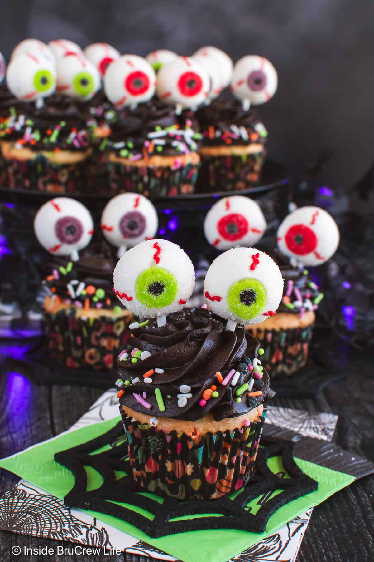 Cupcakes with chocolate frosting and Halloween sprinkles, topped with bloodshot candy eyeballs on sticks