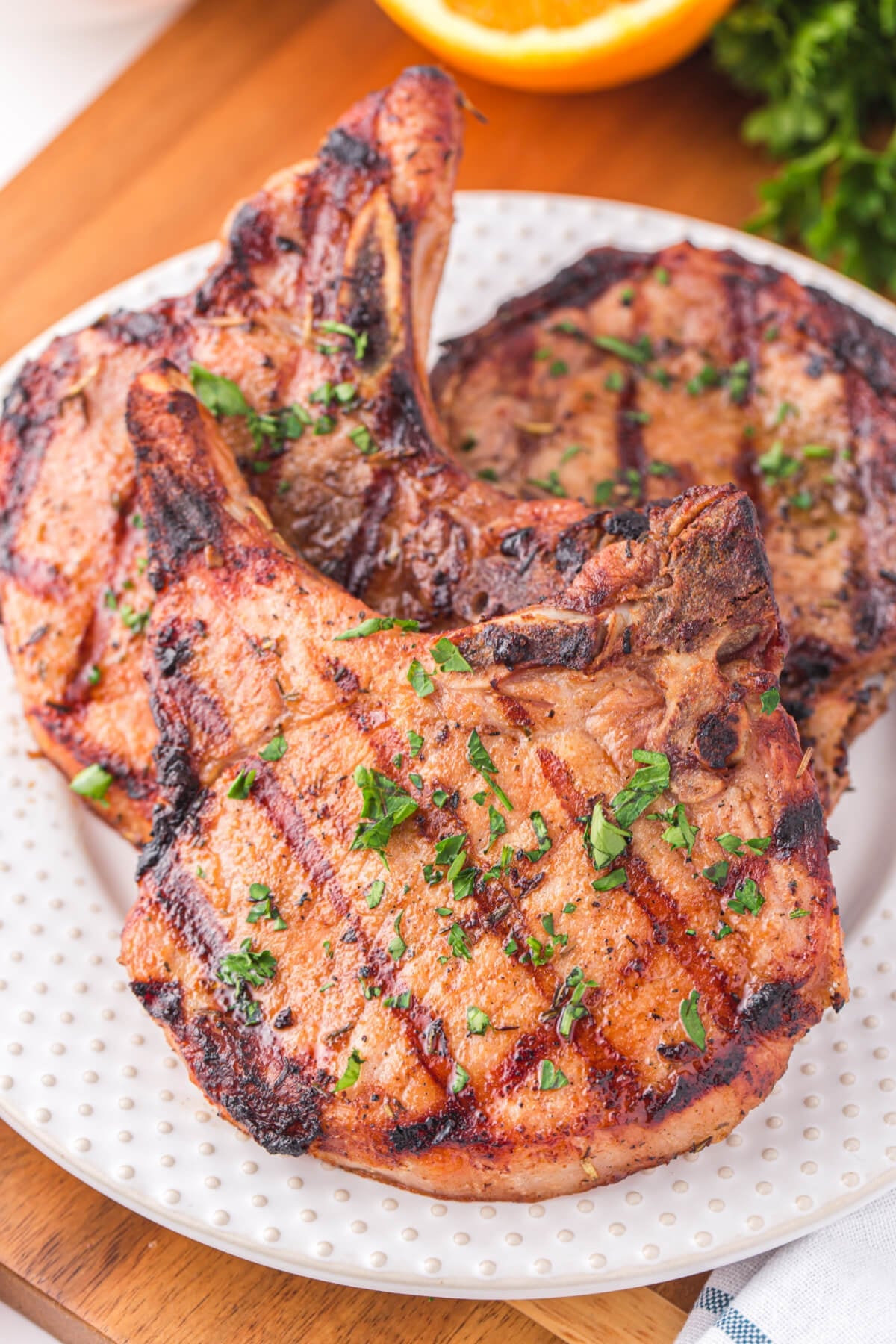 Grilled Pork Chops Thick grilled bone-in pork chops with crosshatch char marks and chopped parsley on a white plate