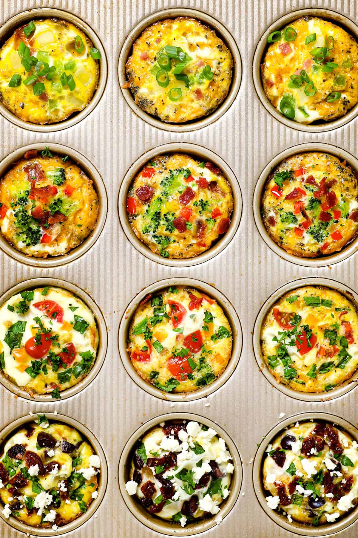 Muffin tin of baked egg muffin cups with tomatoes, peppers, ham, herbs, feta and olives in rows
