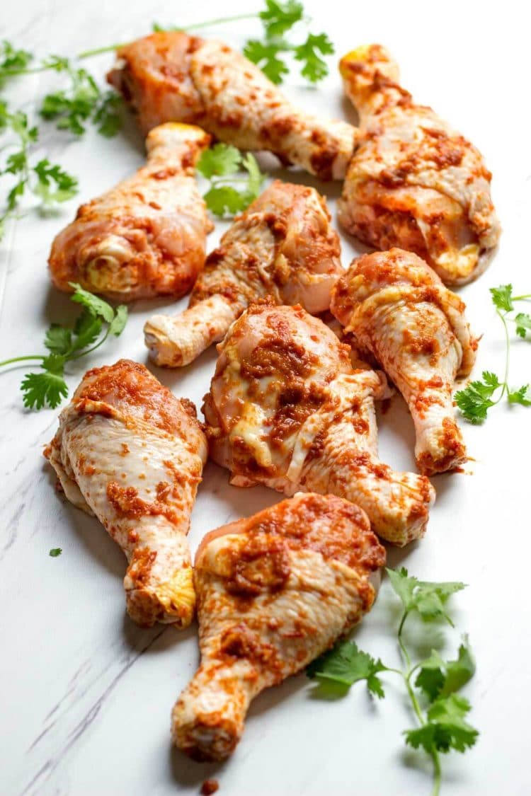 Chicken drumsticks coated in a red honey harissa marinade with fresh cilantro on white marble